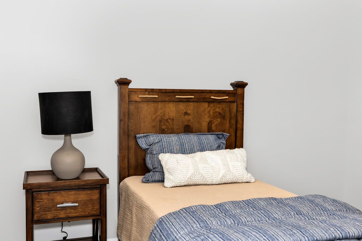 Bedroom with a wooden headboard, nightstand, lamp, and bed with pillows and blanket.