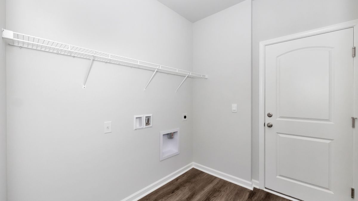 Empty laundry room with white walls, wire shelf, door, and water hookups.