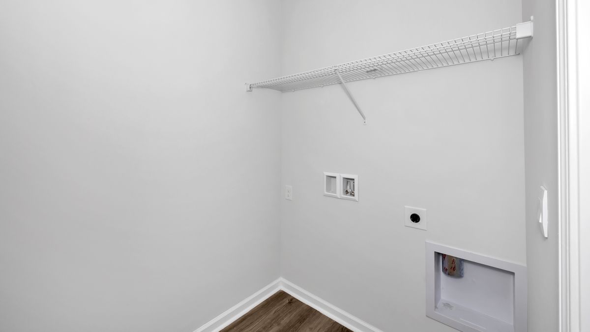 Empty laundry room with wire shelf, electrical outlets, and a floor vent.