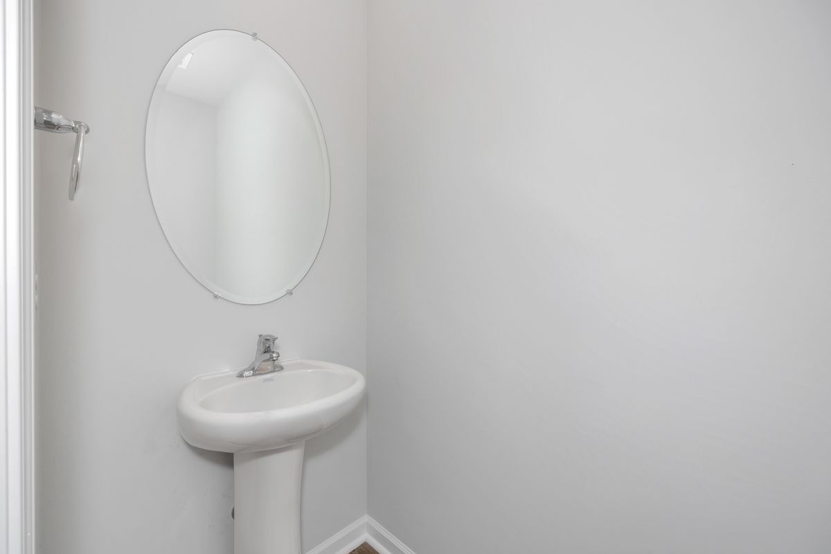 Small bathroom with oval mirror above a pedestal sink. Light gray walls, chrome faucet and towel rack.