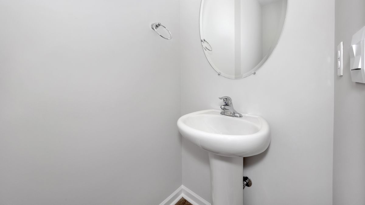 White pedestal sink with faucet, oval mirror, and paper towel dispenser in a small room.