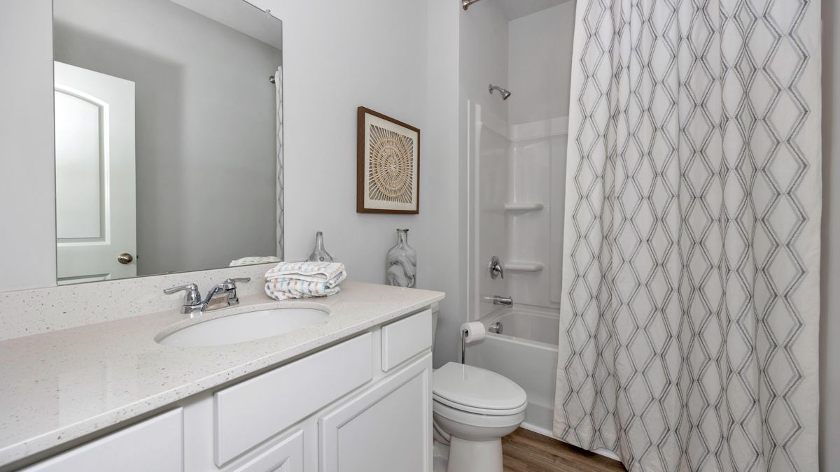 Bathroom with white vanity, toilet, and shower/tub. A white and grey patterned shower curtain hangs.