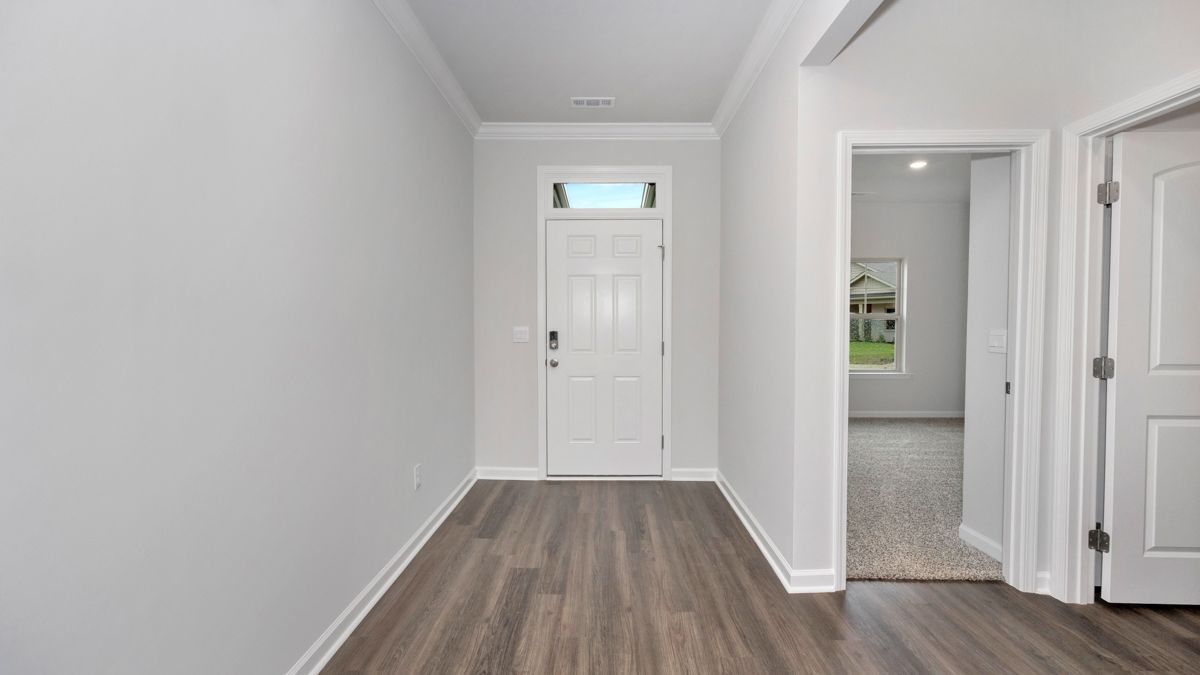 Hallway with a white door, grey walls, wood flooring, and an open doorway to another room.