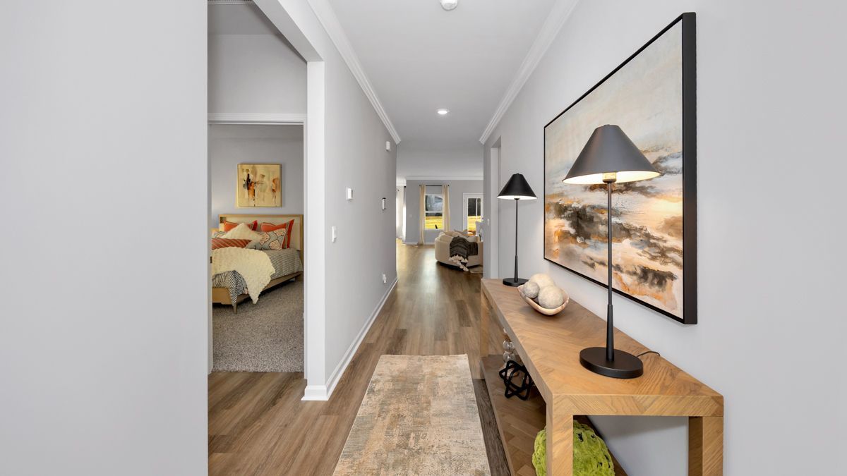 Long hallway with gray walls, wooden console table, lamp, and artwork. Bedroom visible on the left.