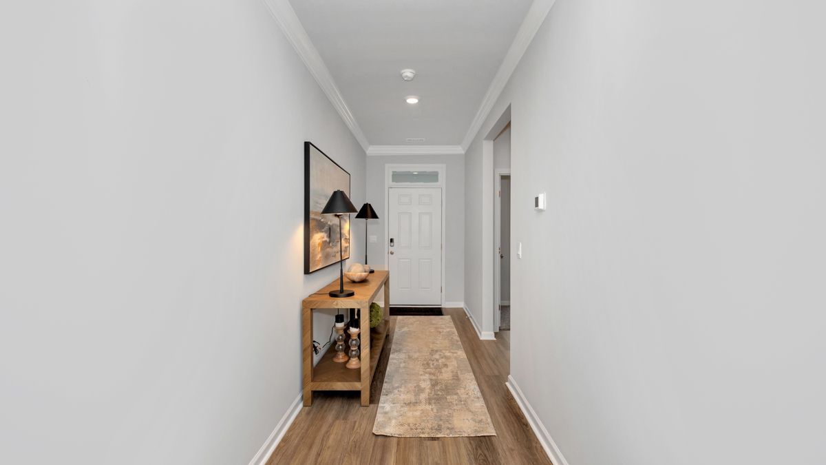 Narrow hallway with wooden console table, art, rug, and door. Gray walls, wood floor.