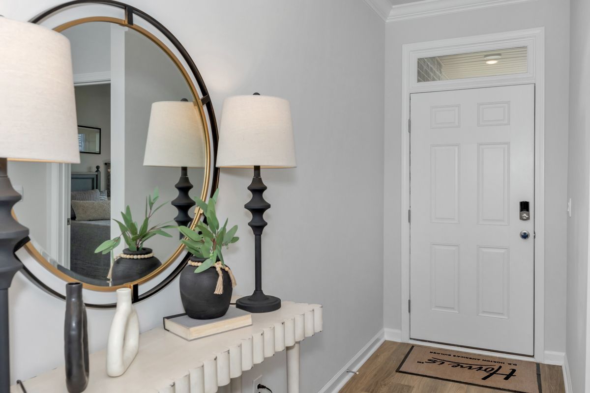 Entryway with a round mirror, console table, lamps, plants, and a white front door.