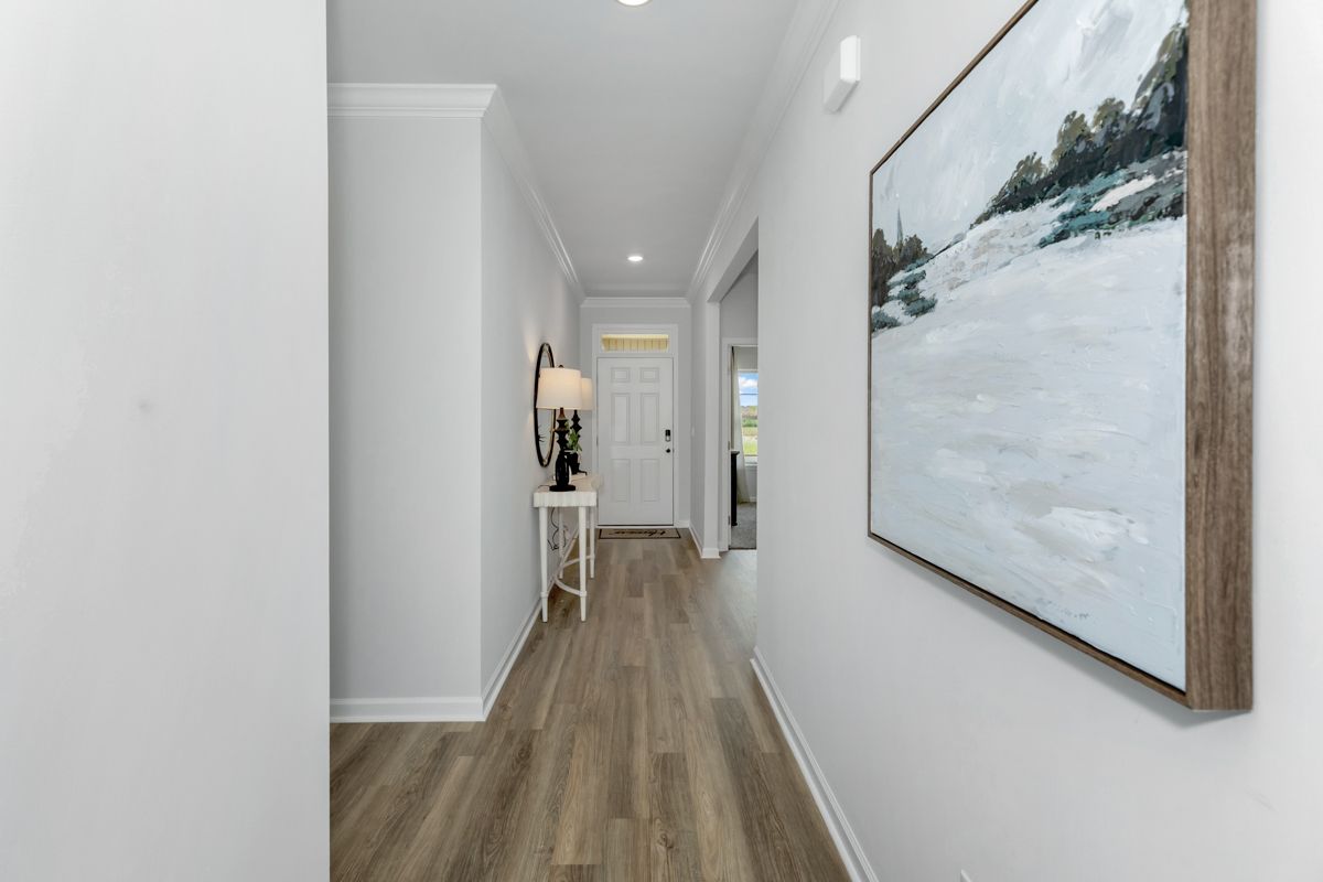 Hallway with light gray walls, wood-look floor, artwork, small table with mirror, and white door.