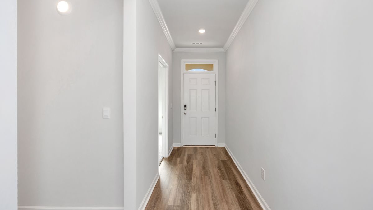 Narrow hallway with light wood-look floors, white walls, and a white door at the end.