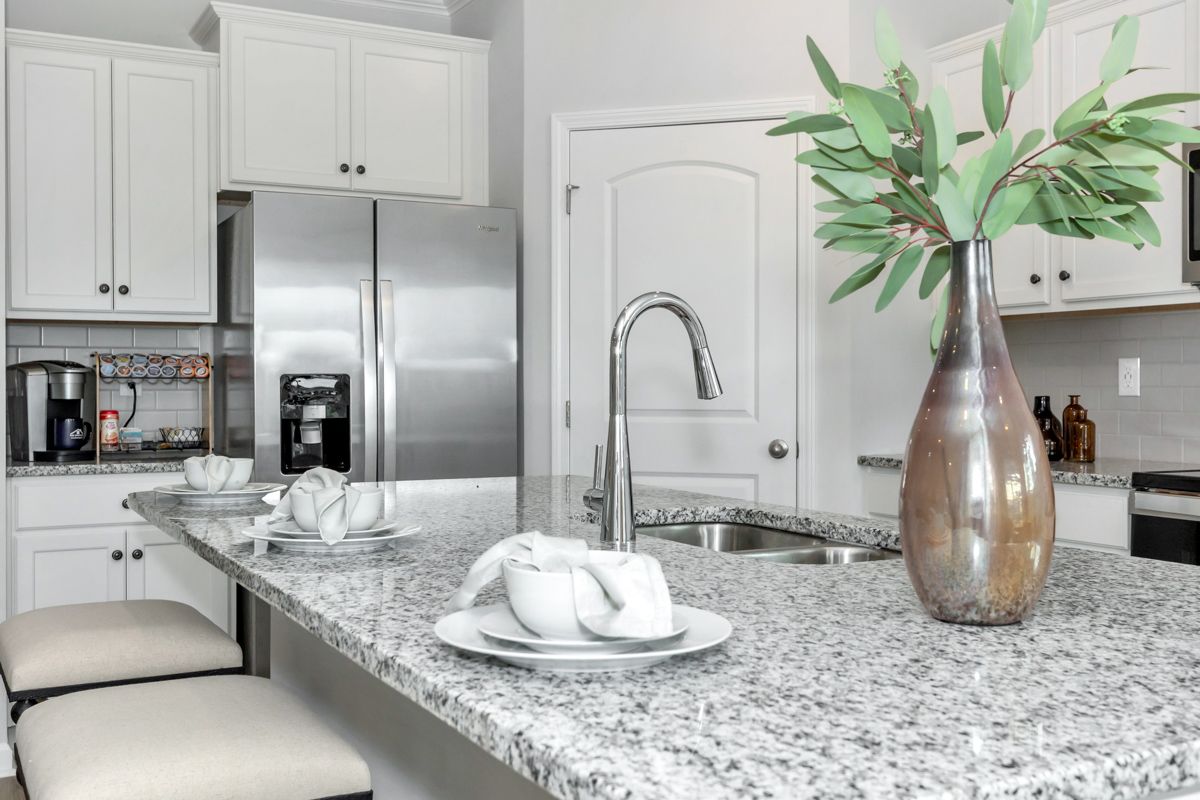 Modern kitchen with granite countertops, stainless steel appliances, and a vase of green branches.