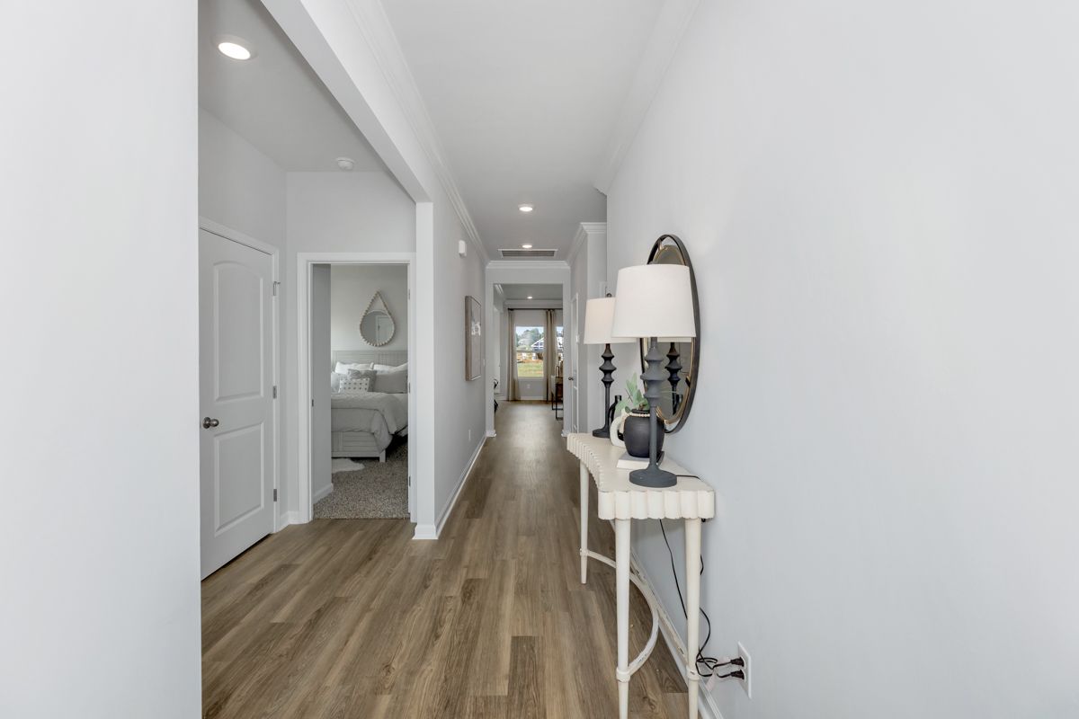 Long hallway with white walls and wood flooring, console table with lamp and mirror.