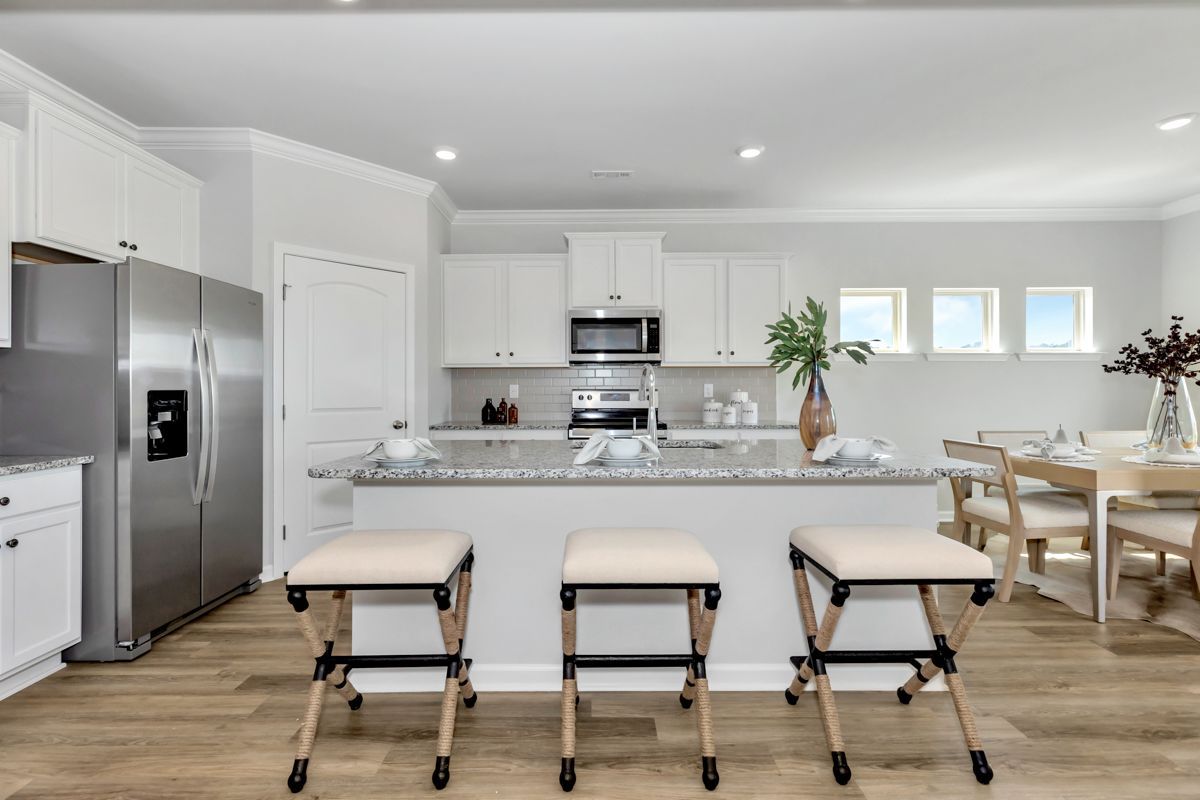 Bright kitchen with white cabinets, stainless steel appliances, and a granite island with three stools.