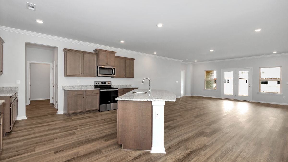 Empty kitchen with light wood cabinets, island, stainless appliances, and French doors.