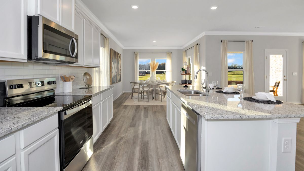 Bright kitchen with white cabinets, granite counters, stainless steel appliances, and a view to the dining area.