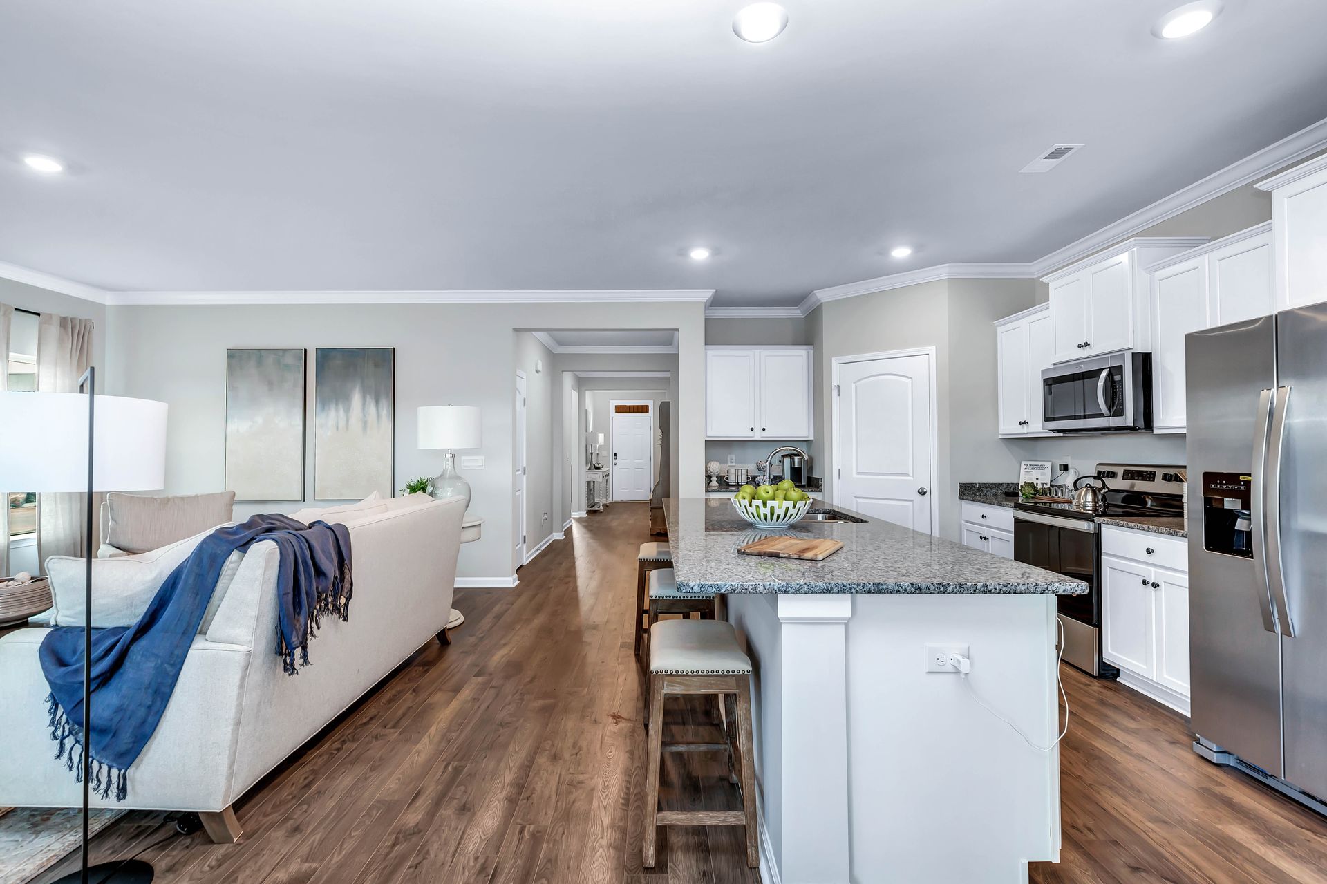 Open-concept kitchen and living room with white cabinets, island with seating, stainless steel appliances, and a couch.