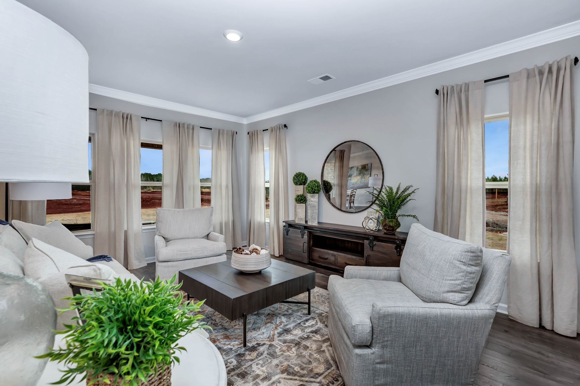 Living room with gray and neutral tones; sofa, chairs, coffee table, large mirror, and windows.