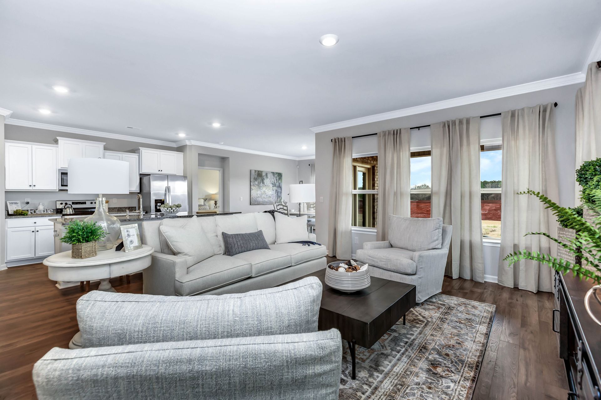 Open-plan living room with light-colored walls, furniture, and a view through three windows.