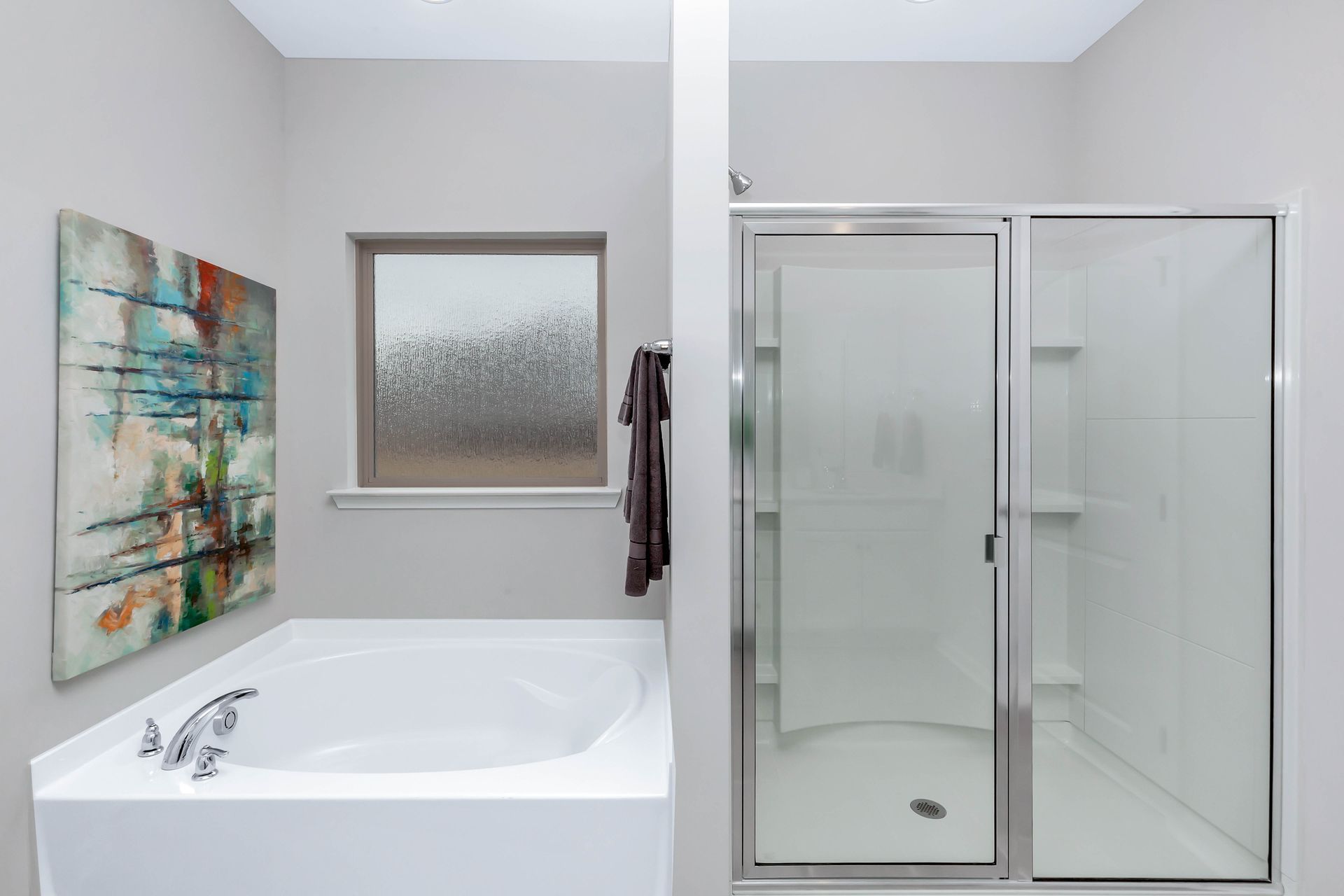 Bathroom with a white tub, shower, window with textured glass, and an abstract painting.