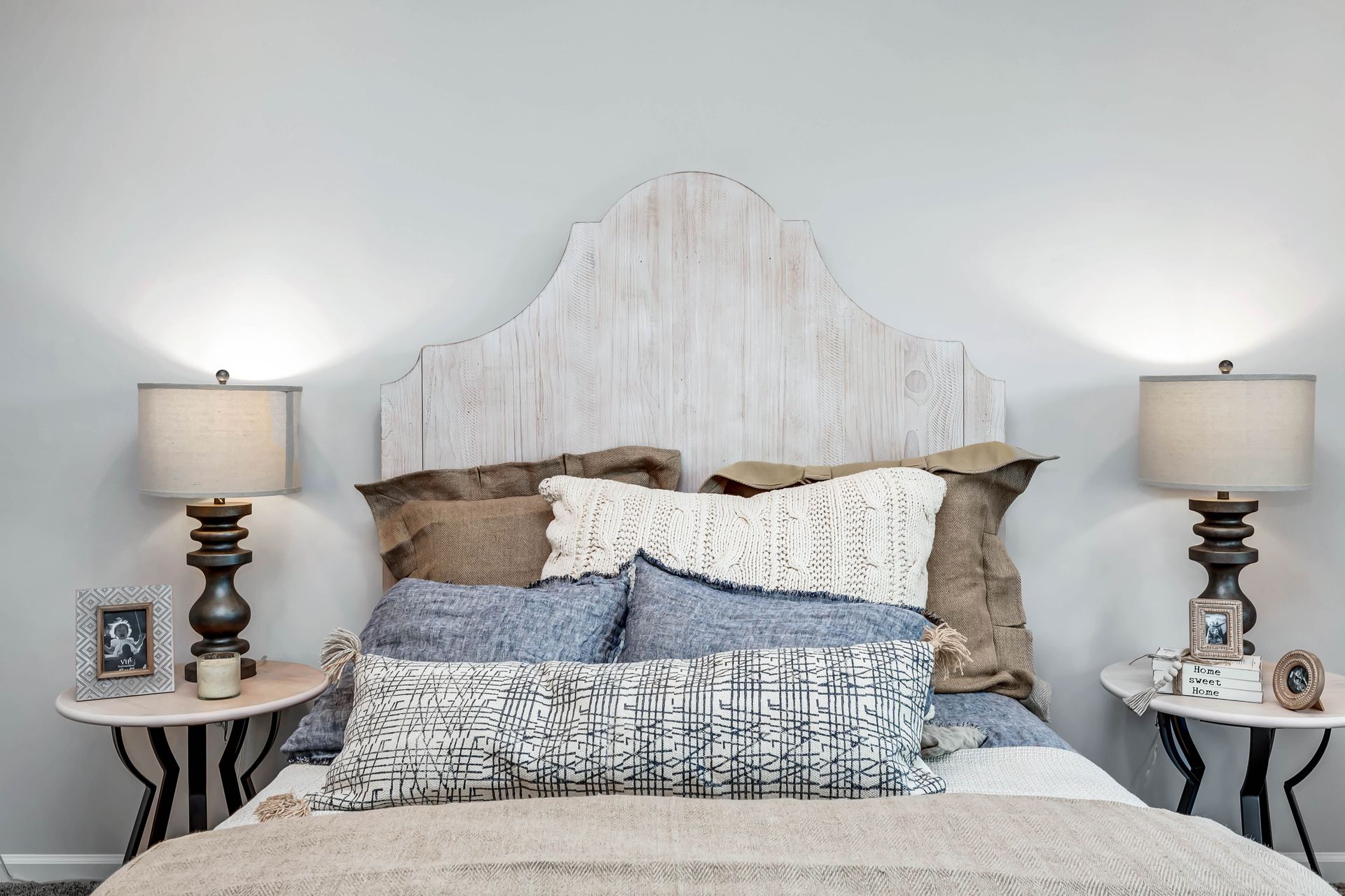 Bedroom with whitewashed headboard, lamps on side tables, and layered pillows and bedding.