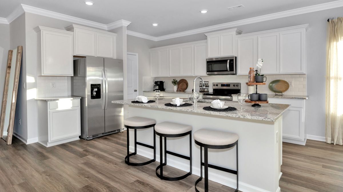 Modern kitchen with white cabinets, stainless steel appliances, island with stools, and hardwood floors.