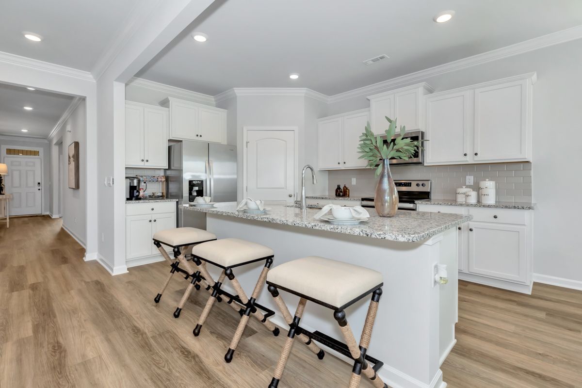 Modern white kitchen with island seating, stainless steel appliances, and light wood floors.