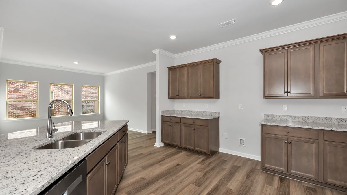 A bright kitchen with brown cabinets, granite countertops, and wood flooring.