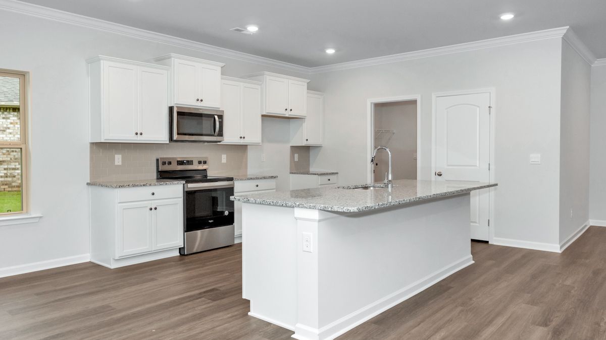 White kitchen with island, cabinets, and stainless steel appliances. Light gray countertops and wood floors.