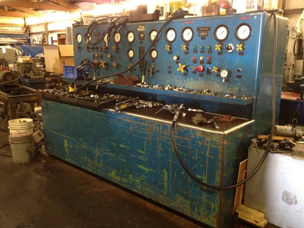 Blue industrial testing machine with gauges and controls, in a workshop setting.