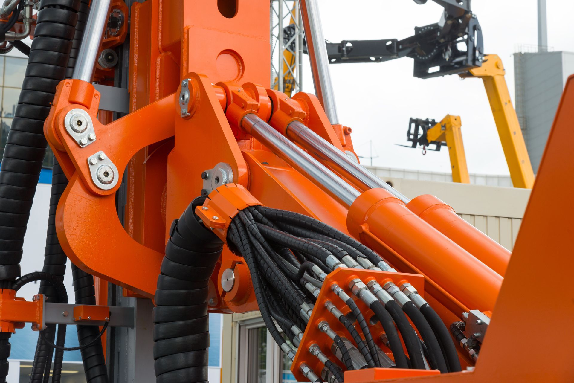 Orange industrial machinery with hydraulic cylinders and bundled black cables in a workshop