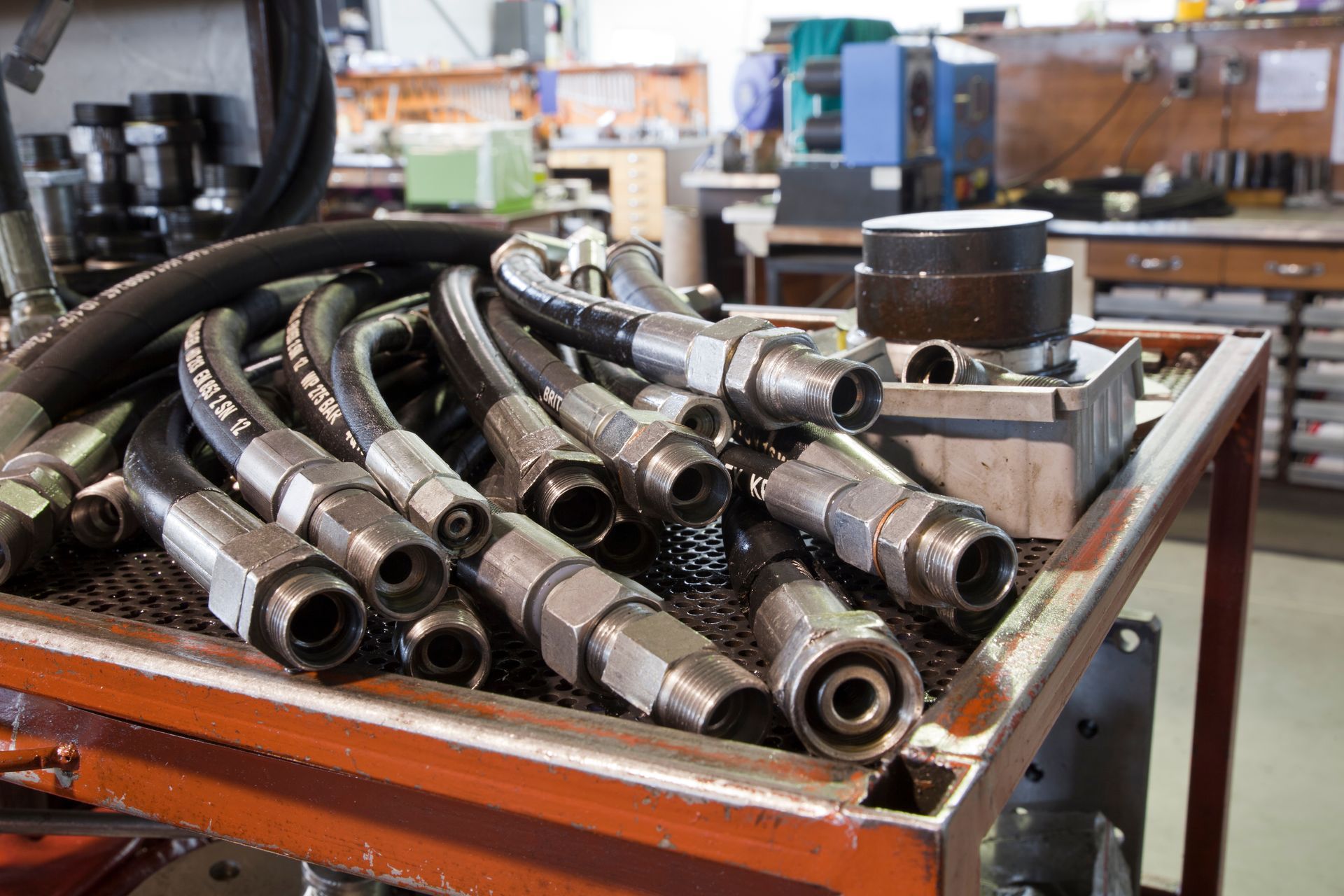 Pile of industrial hydraulic hoses and metal fittings in a workshop cart