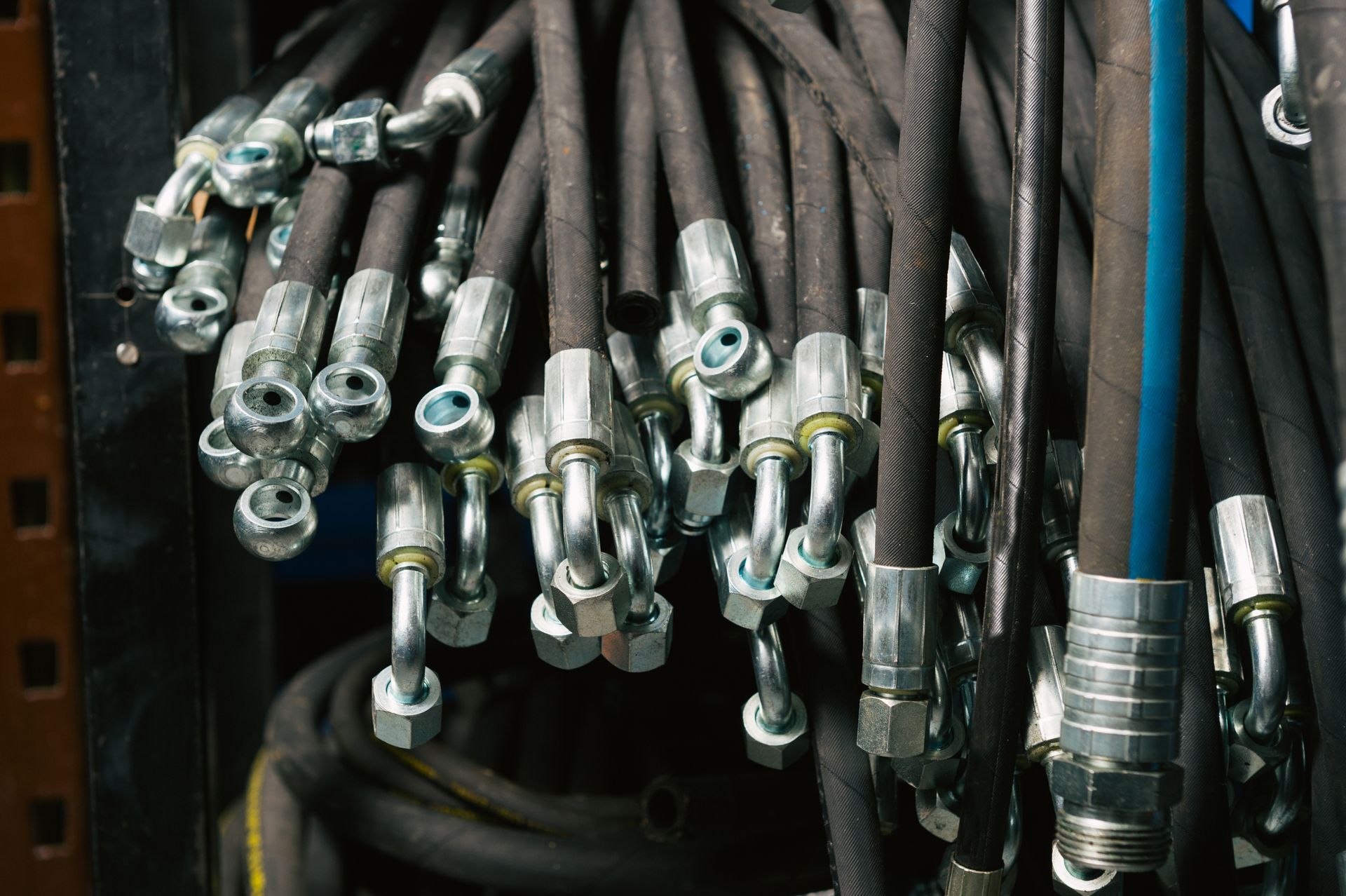 Black hydraulic hoses with silver fittings, hanging closely together.