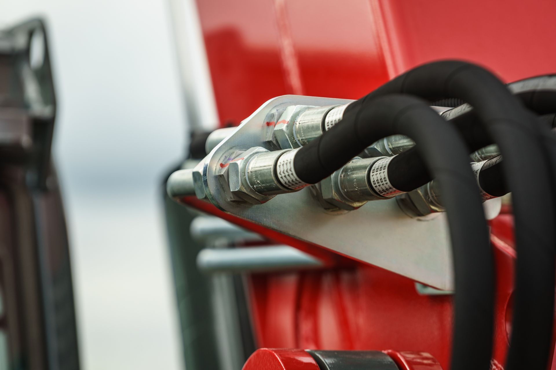 Close-up of hydraulic hoses connected to a red machine, with silver fittings and a light background.
