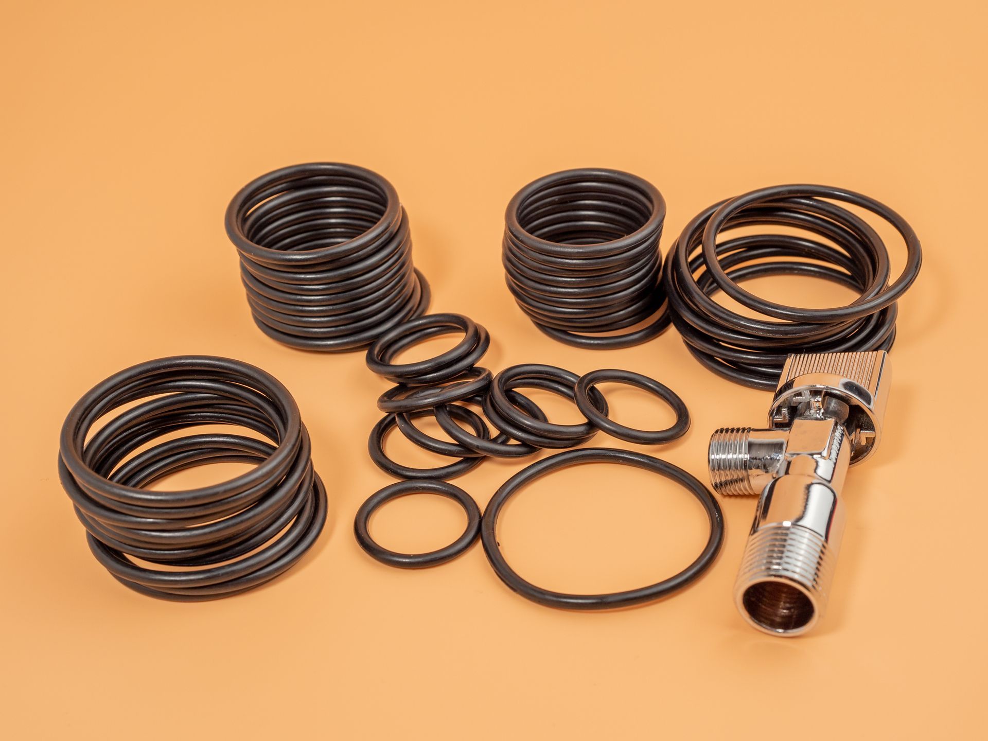 Black rubber O-rings and a chrome faucet on an orange background.