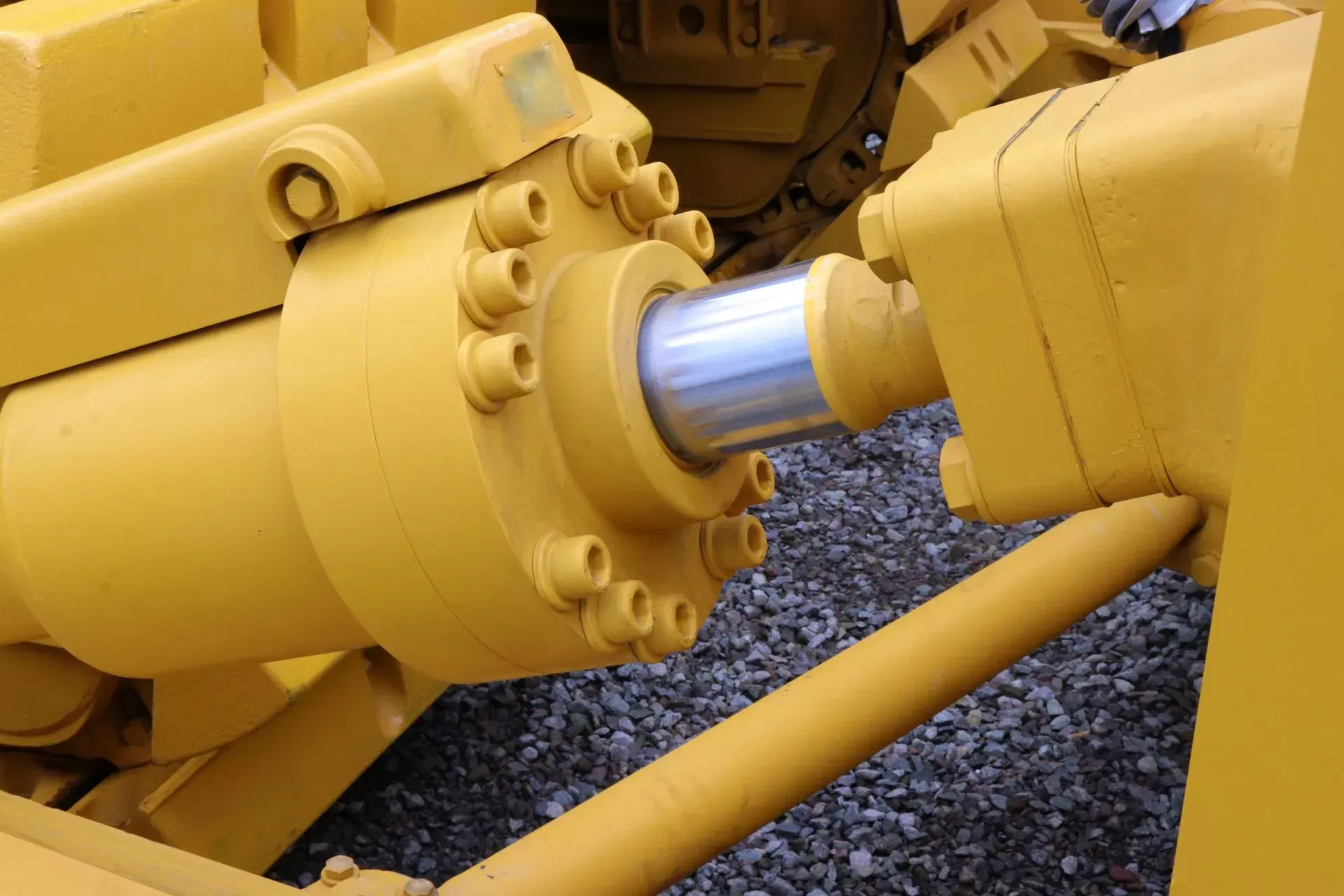 Yellow hydraulic cylinder on heavy machinery, close-up. Shiny metal rod extends from a bolted cylinder.