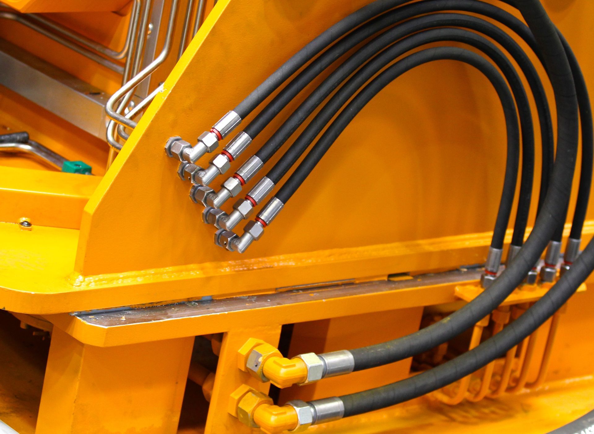 Close-up of yellow industrial machinery with black hydraulic hoses and silver fittings.