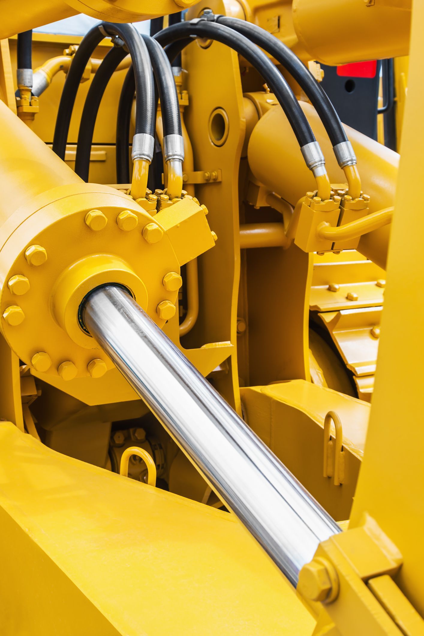 Yellow hydraulic cylinder on heavy machinery with black hoses.