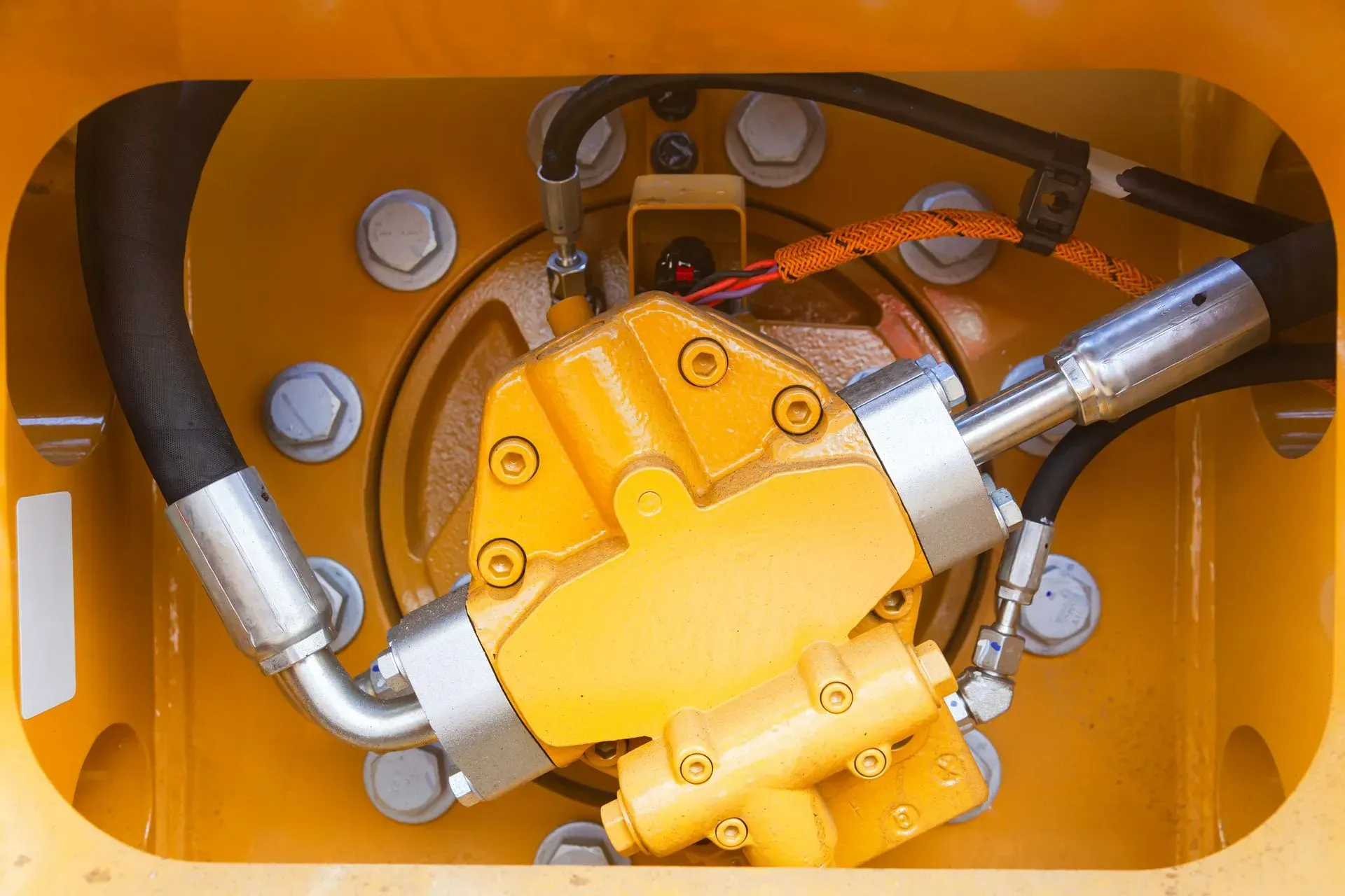 Yellow hydraulic pump with black hoses and silver connectors, mounted inside yellow machine frame.