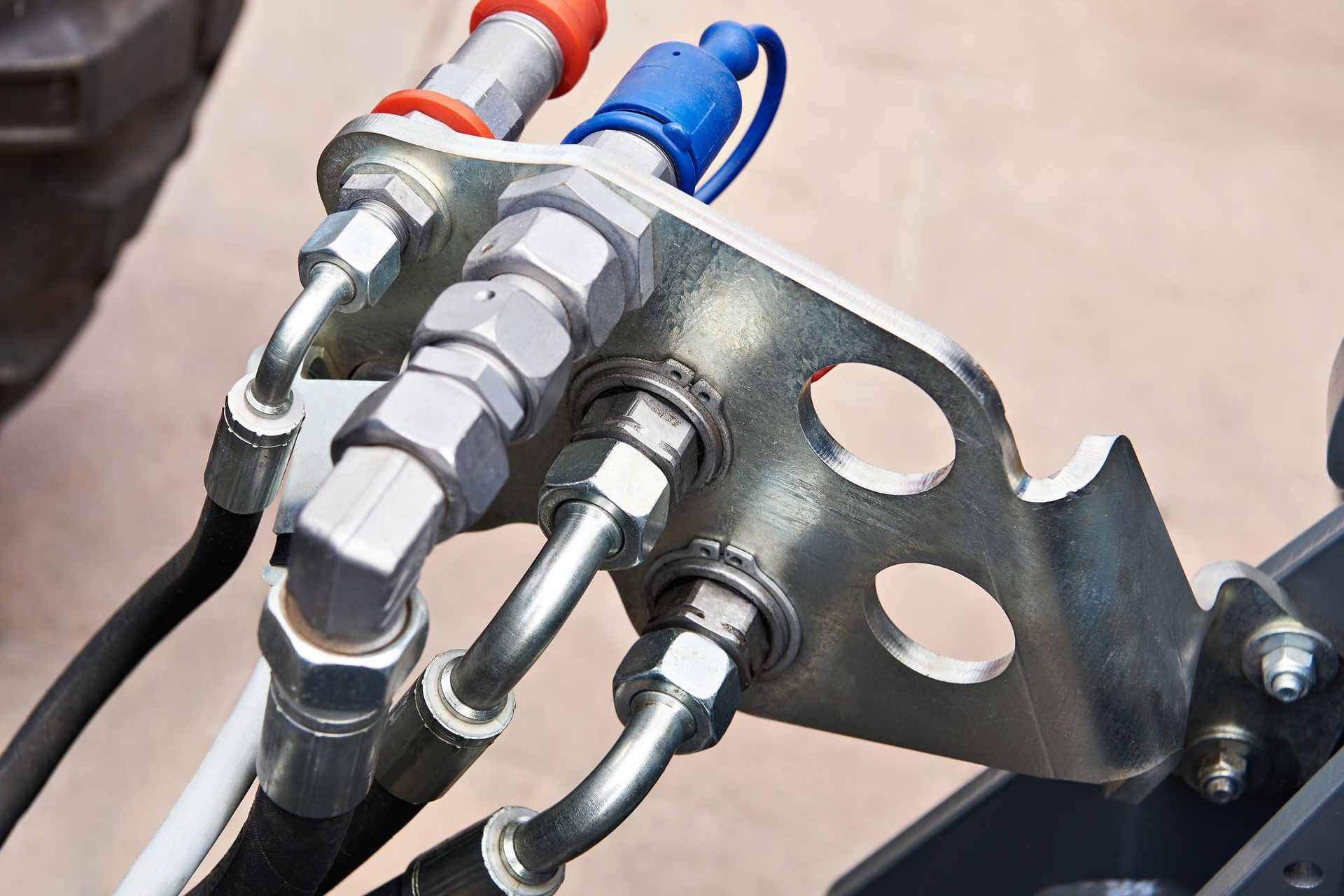 Close-up of hydraulic fittings on a metal bracket, with red and blue caps.