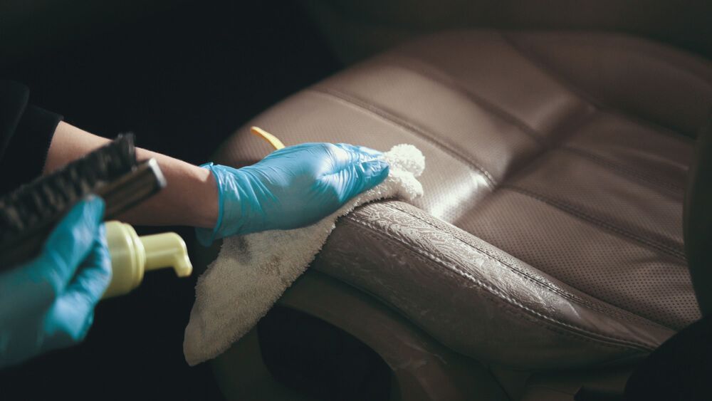 A Person Wearing Blue Gloves is Cleaning a Leather Seat in a Car — On The Move Carpet Cleaning in Burleigh Waters, QLD