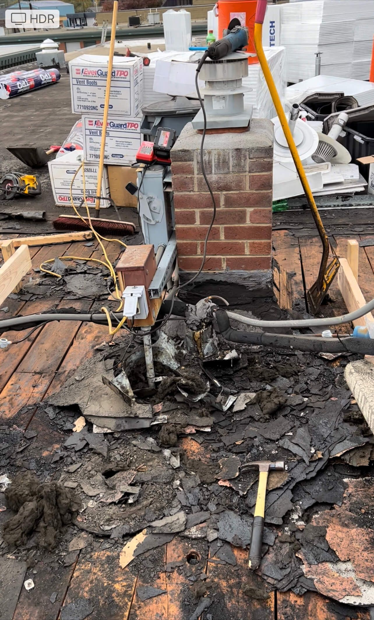 Workers tearing off the old built-up roofing at Labcorp Yakima, with roofing debris and tools on the exposed wooden deck.
