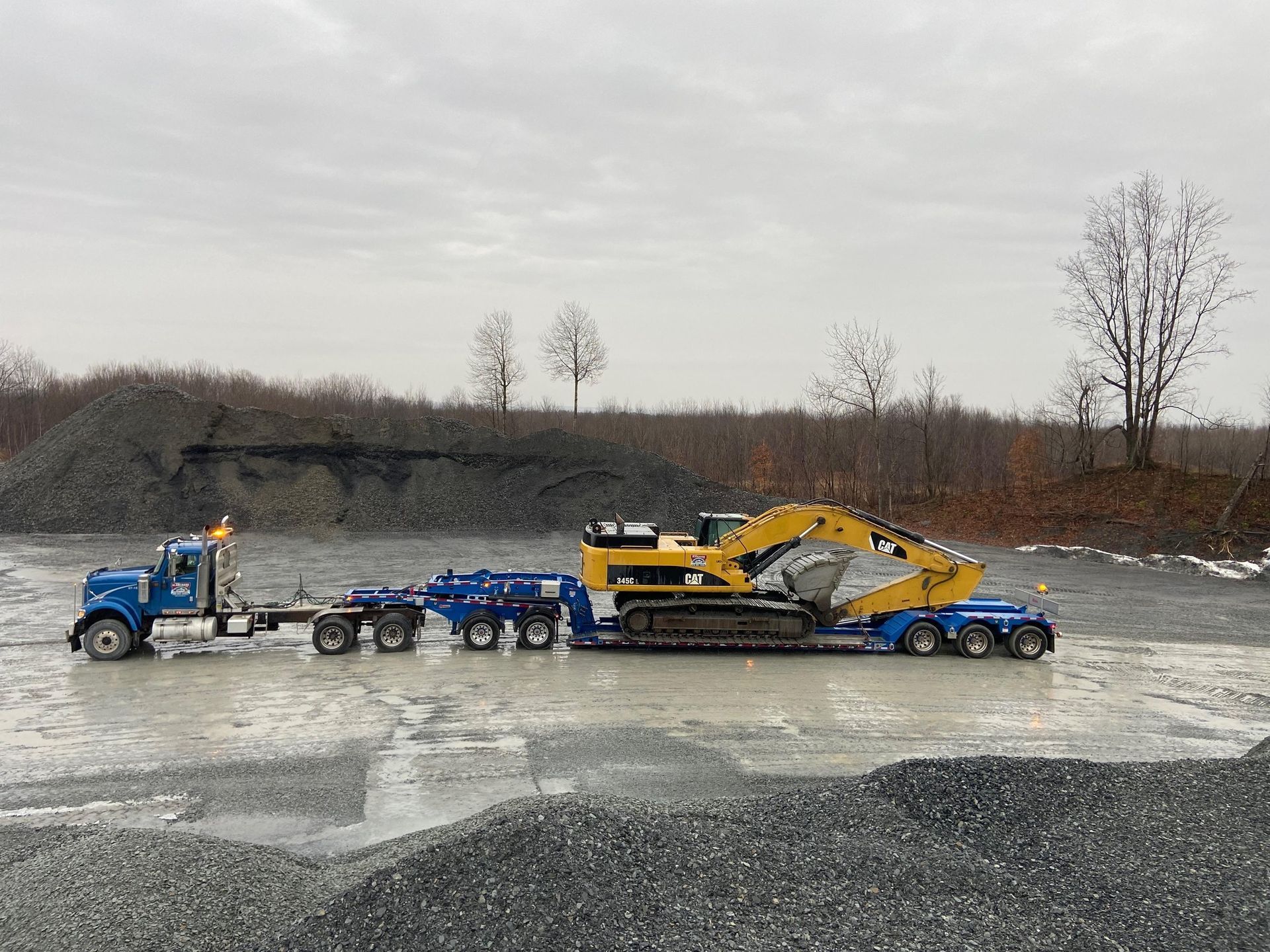 Un camion bleu transporte une excavatrice jaune sur une remorque.