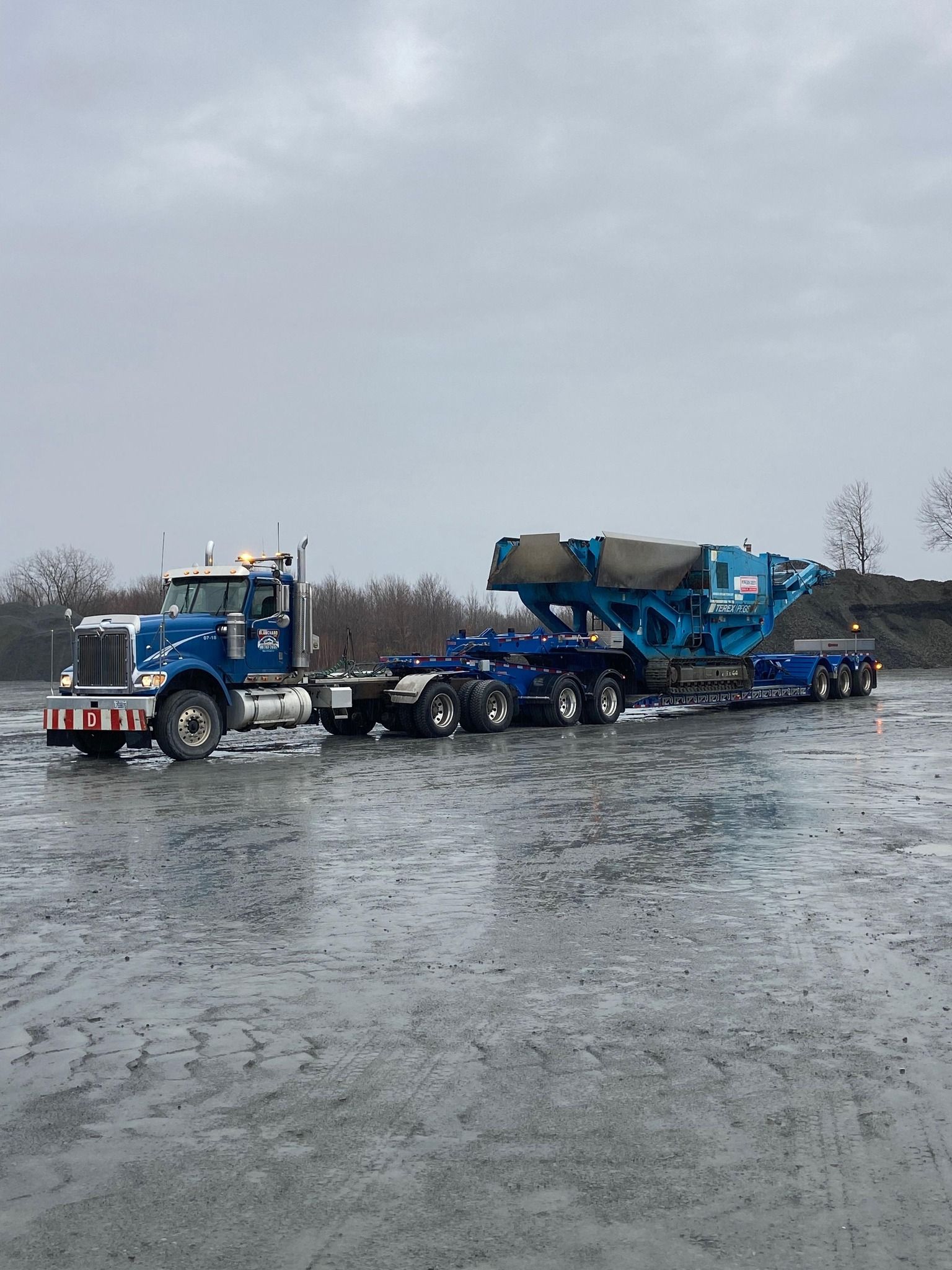 Un semi-remorque bleu transporte une grosse machine bleue sur une remorque.