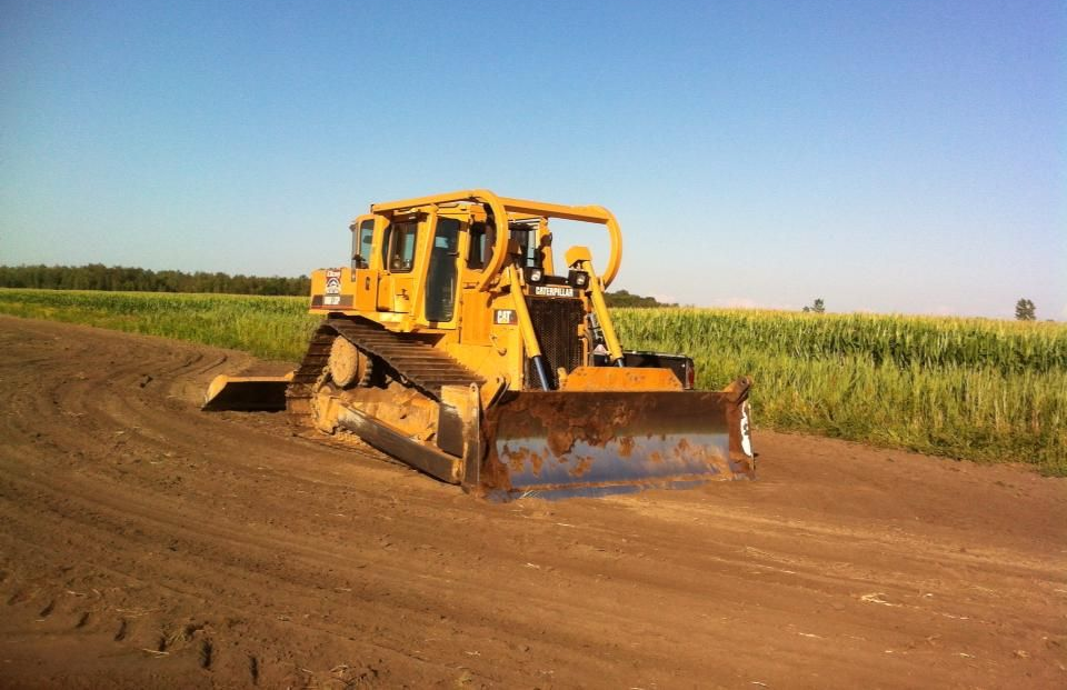 Un bulldozer roule sur un chemin de terre dans un champ.