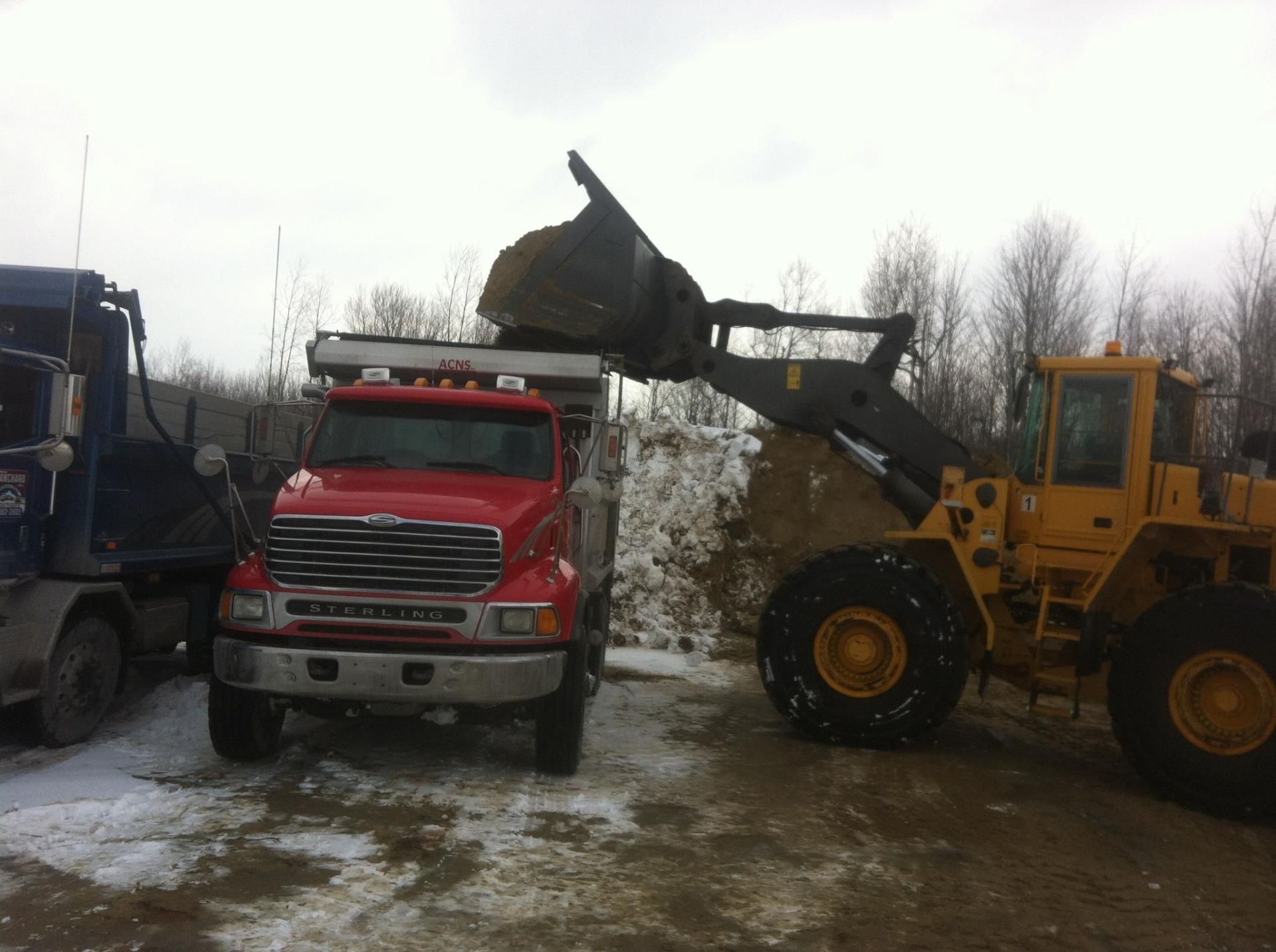 Un camion rouge est chargé de terre par un bulldozer jaune.