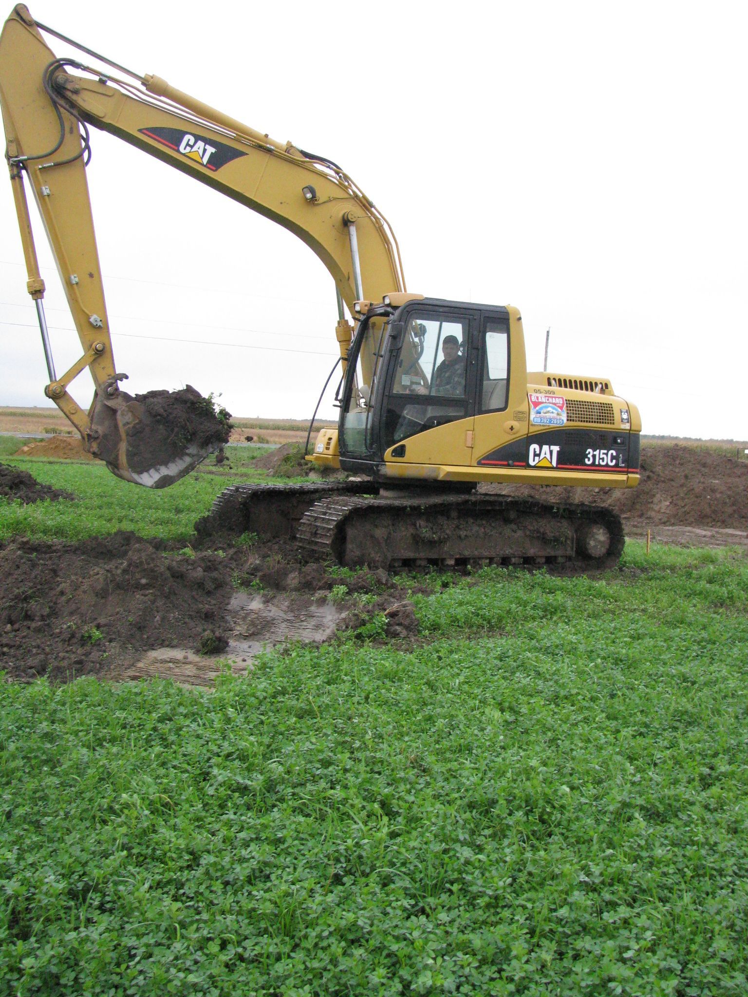 Une excavatrice jaune creuse un trou dans un champ herbeux.