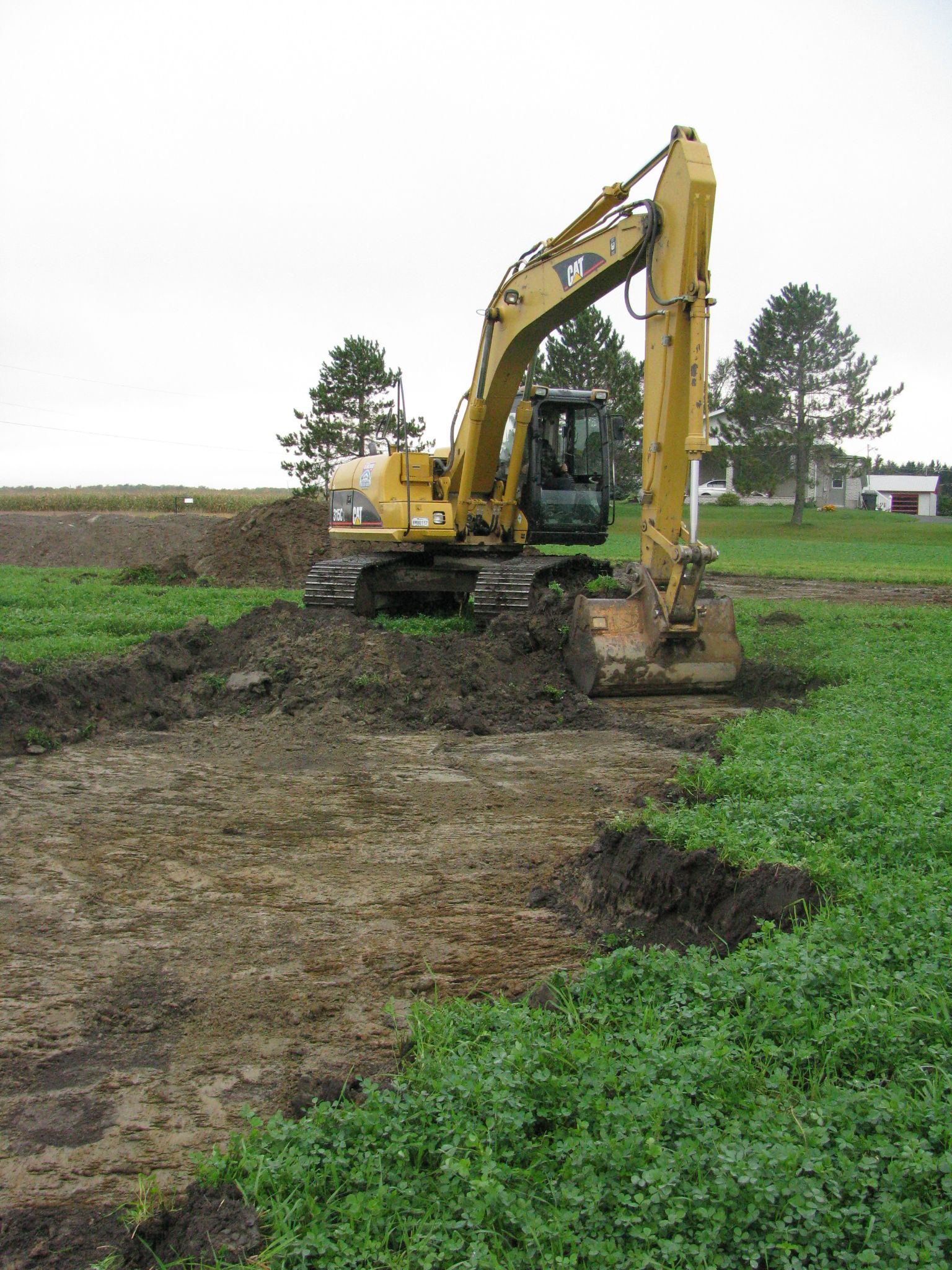 Une excavatrice jaune creuse un trou dans un champ.