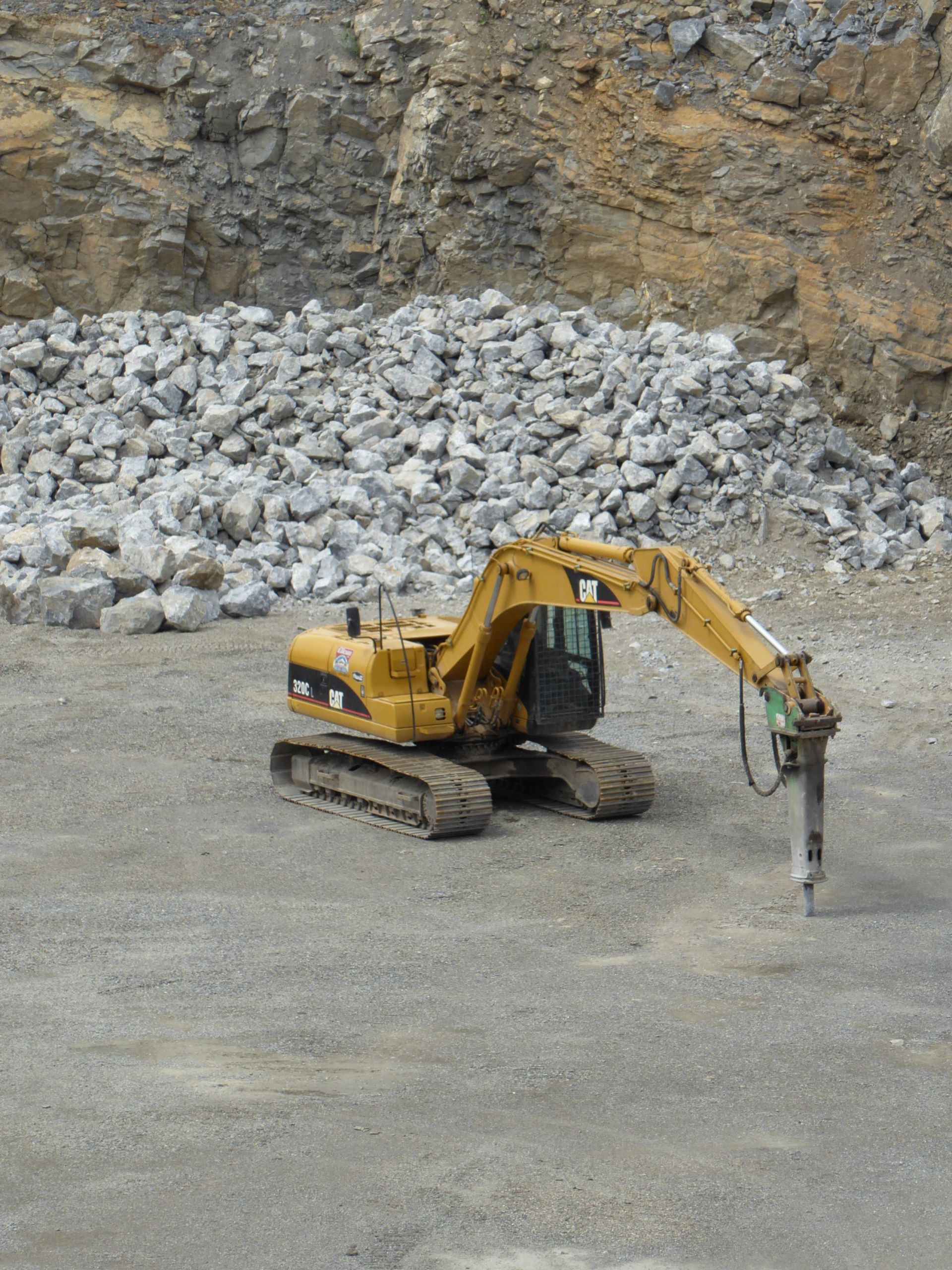 Une excavatrice jaune avec un marteau attaché est assise dans un tas de rochers.