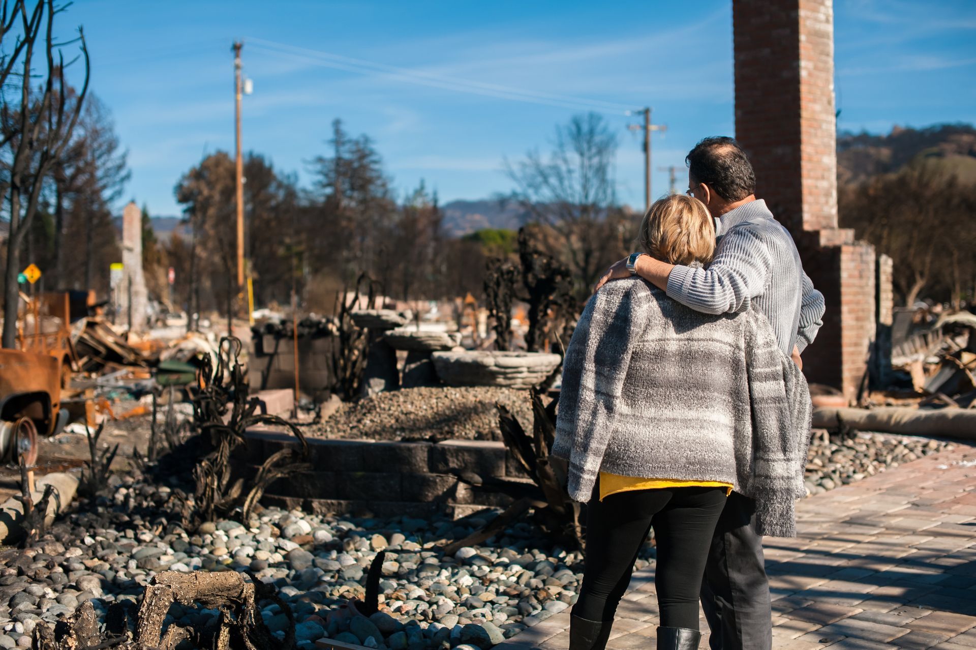 couple embraces while looking over rubble of burnt down home