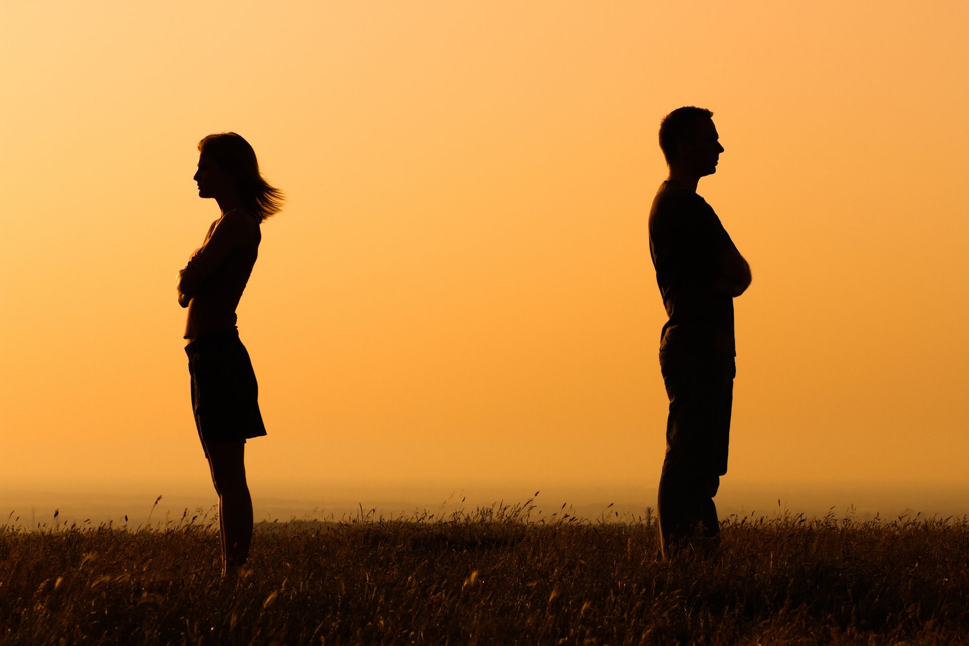 A man and a woman are standing in a field with their arms crossed