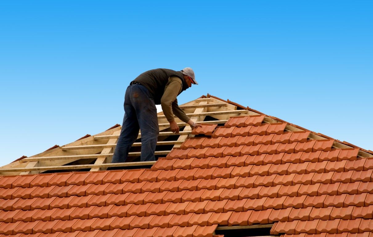 Roofer installing clay tiles on a house roof under a clear blue sky.