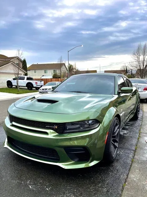 Green Dodge Charger parked on a residential street under a cloudy sky.